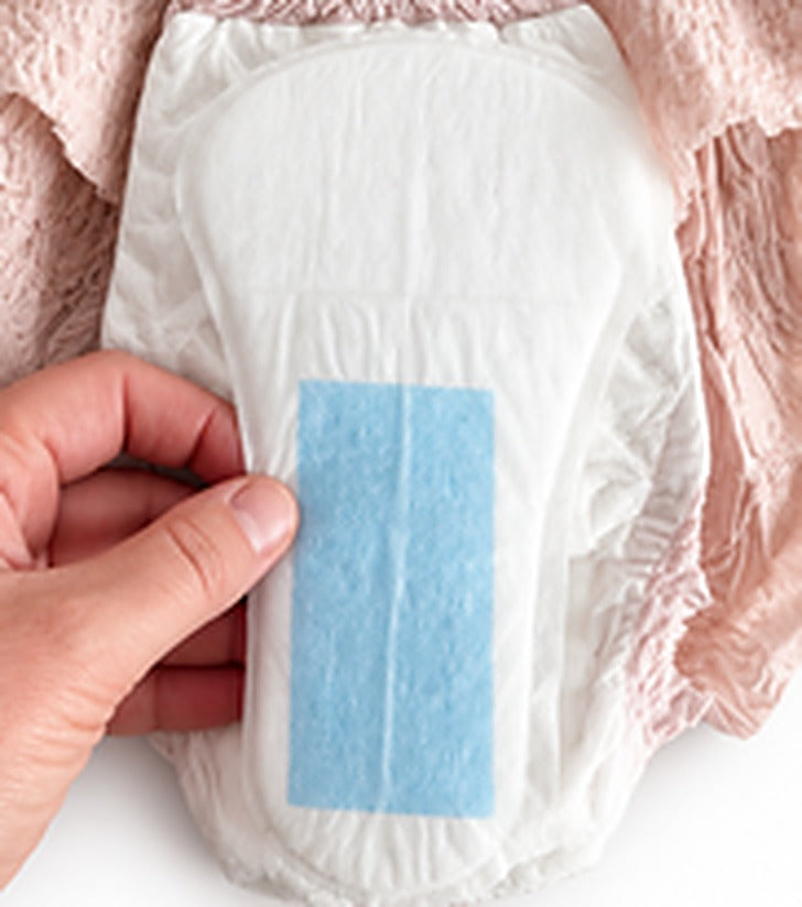 A hand placing the UraGuard shield, blue panel up, inside the front of a pink pull-up brief